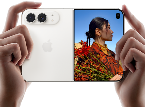 iPhone Duo, finition blanc stellaire, tenu à deux mains en position horizontale, déplié, le volet extérieur gauche présente les caméras arrière Fusion 48 MP, le volet extérieur droit présente l’écran externe affichant une personne qui se fait photographier et peut voir son propre visage pendant la prise de vue à l’aide de Duo Preview