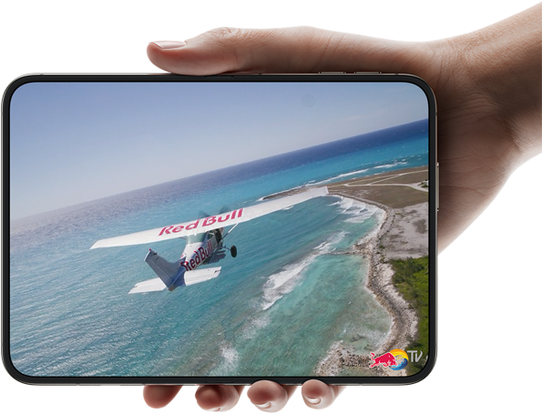 iPhone Duo, tenu d’une main, ouvert en mode paysage, entièrement déplié, l’écran interne affiche la photo d’un avion survolant une plage.