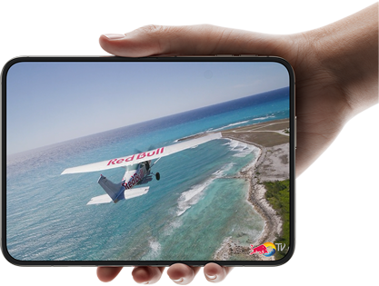 iPhone Duo, tenu d’une main, ouvert en mode paysage, entièrement déplié, l’écran interne affiche la photo d’un avion survolant une plage.