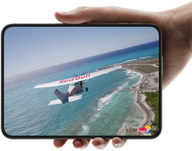 iPhone Duo, tenu d’une main, ouvert en mode paysage, entièrement déplié, l’écran interne affiche la photo d’un avion survolant une plage.